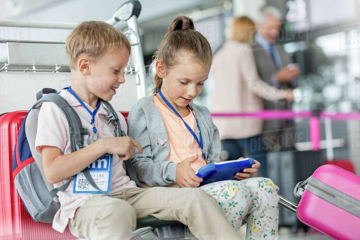 Brother and sister using digital tablet in airport departure area Stock Photo Dissolve