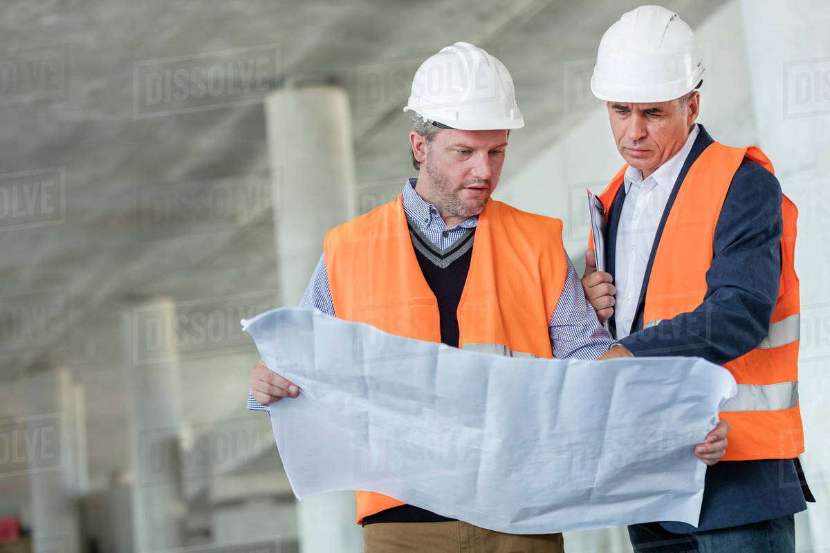Male engineers examining underground blueprints at construction site ...