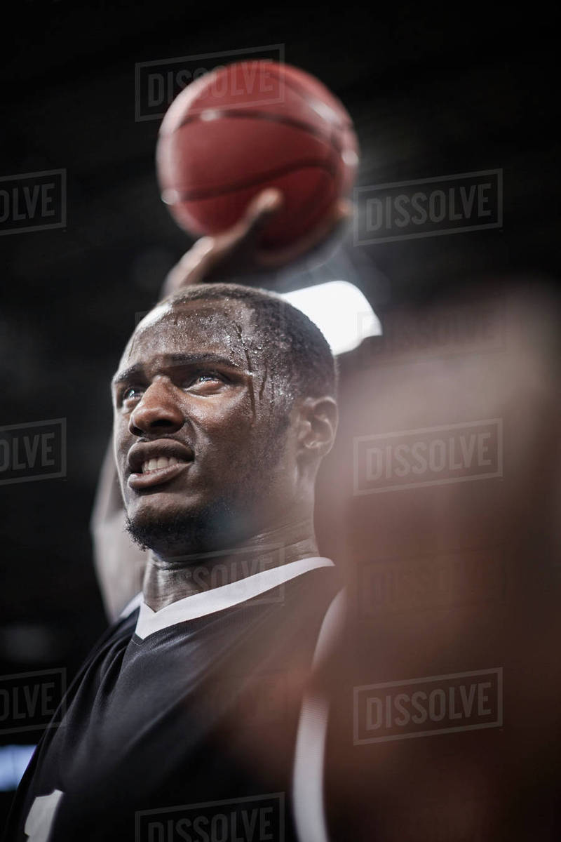 serious sweating basketball player holding basketball overhead