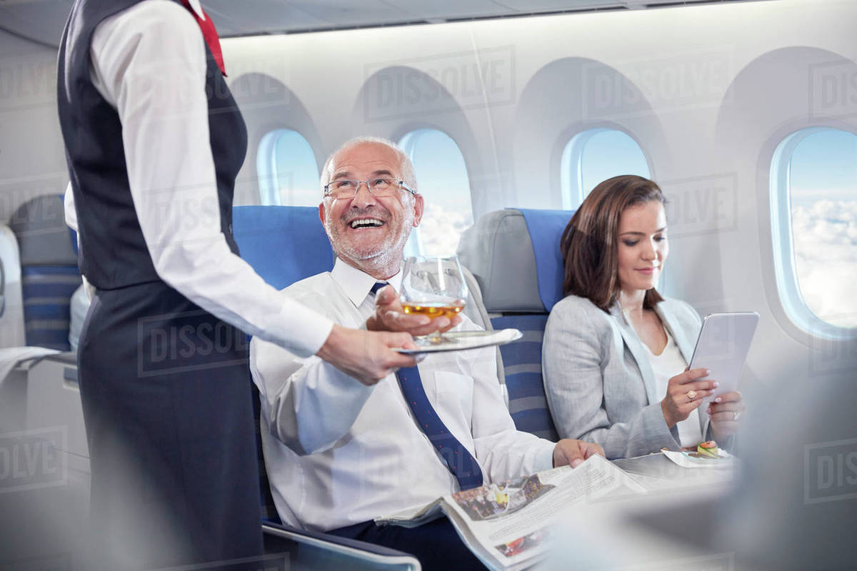 Flight attendant serving whiskey to smiling businessman riding in first  class on airplane - Stock Photo - Dissolve