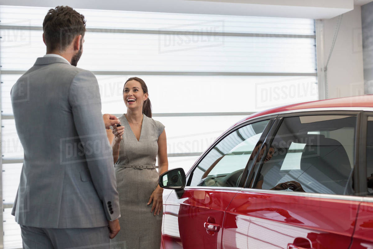 Car salesman giving keys to new car to female customer in car