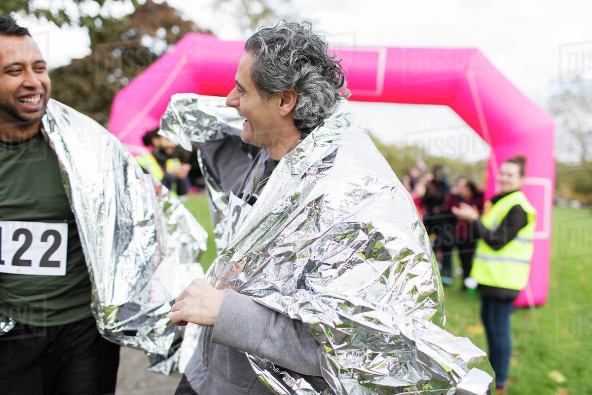 Smiling male marathon runners finishing race, wearing thermal blankets Stock Photo Dissolve