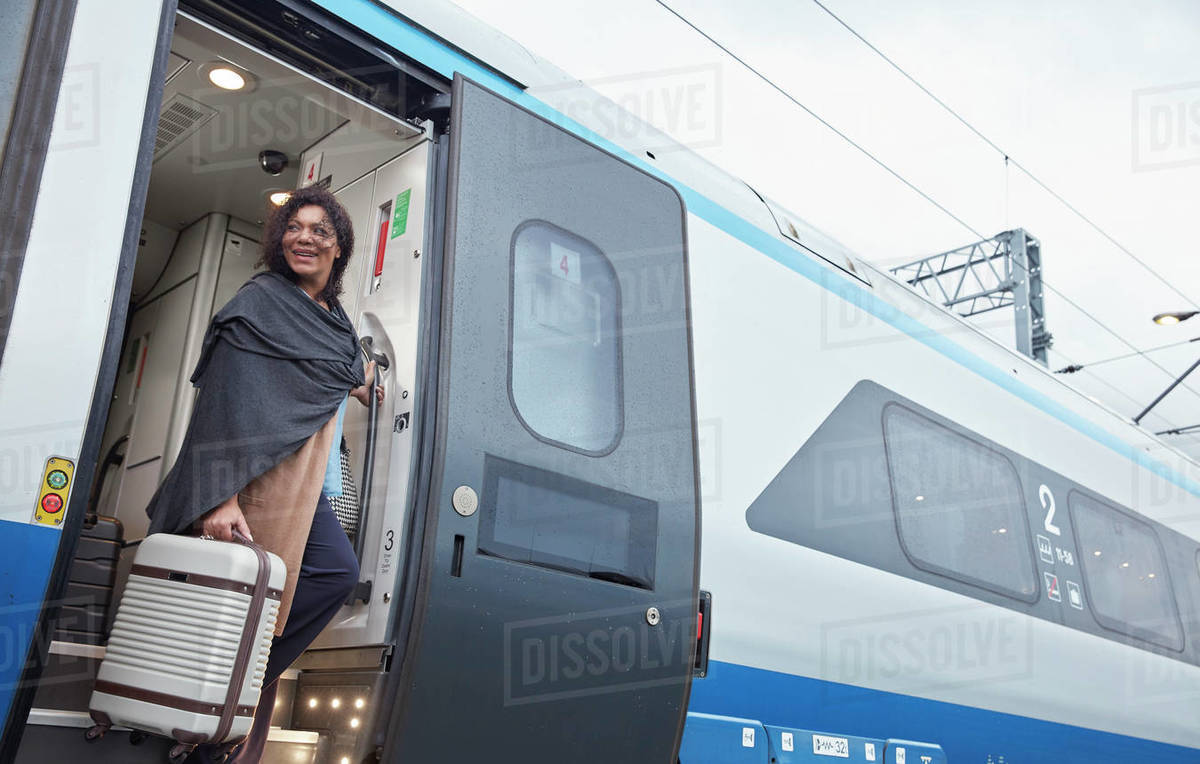 Woman with suitcase getting off passenger train at train station