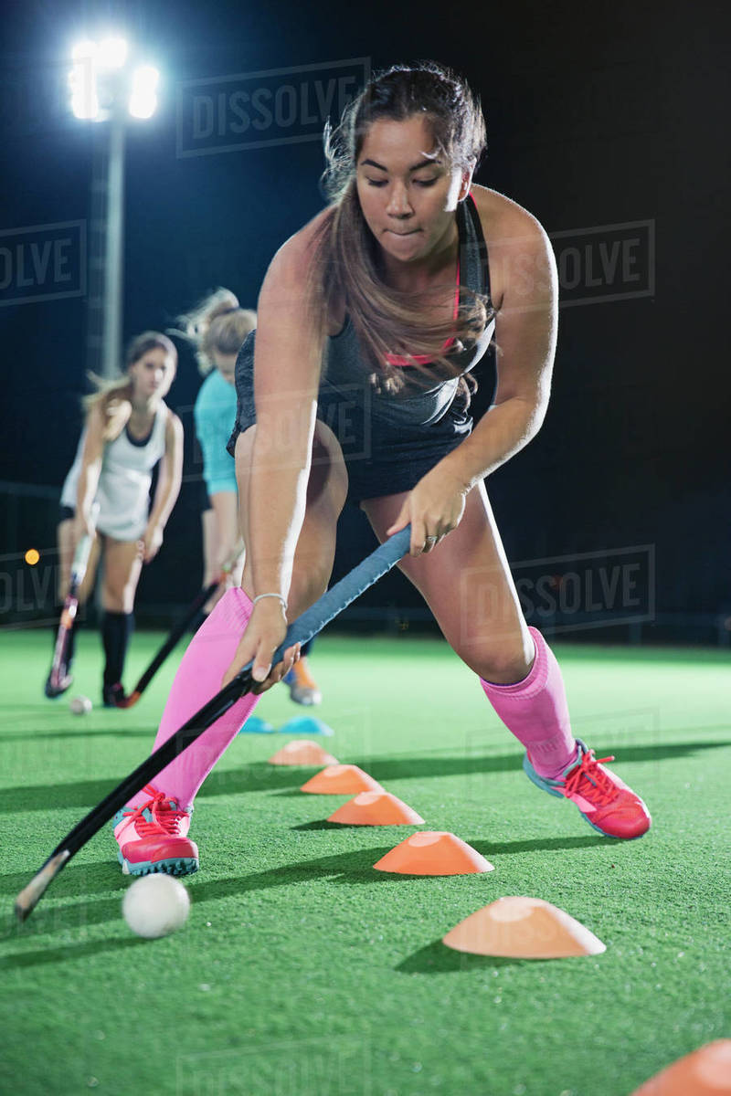 Focused young female field hockey player practicing sports drill on