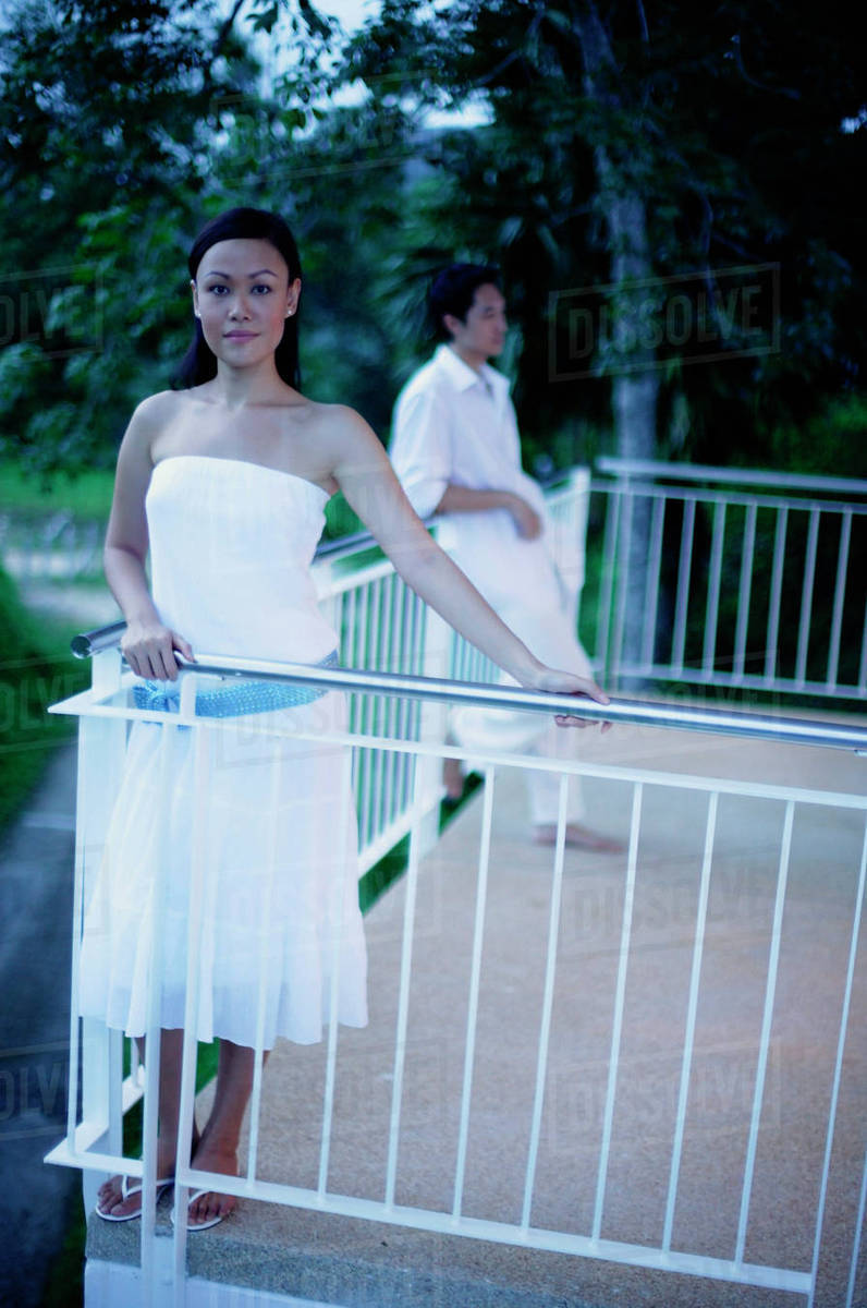 Woman standing on balcony, man leaning on railing in the background ...