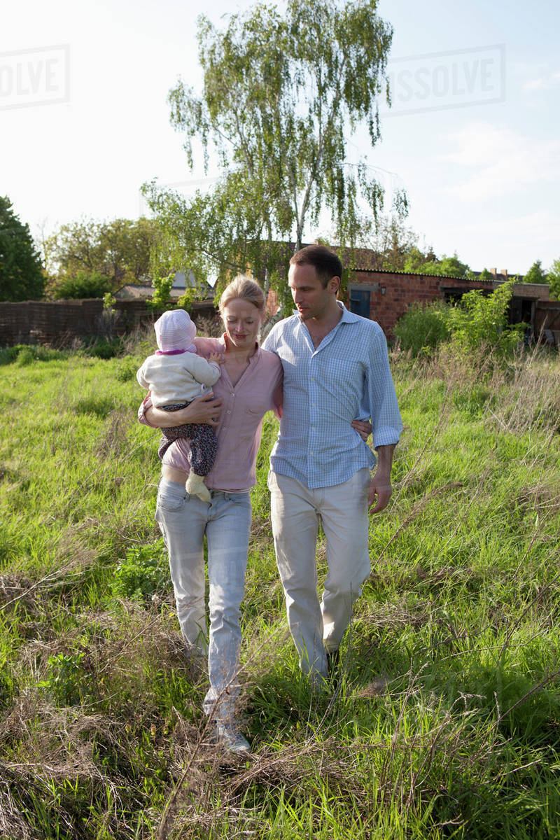 A man and a woman holding a baby walking in back of their country
