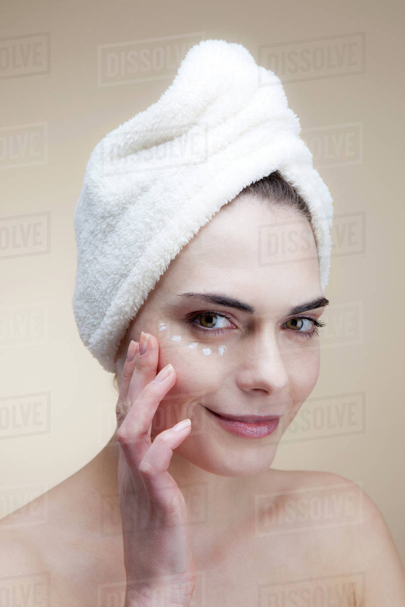 A smiling young woman applying moisturizer under her eye Stock Photo