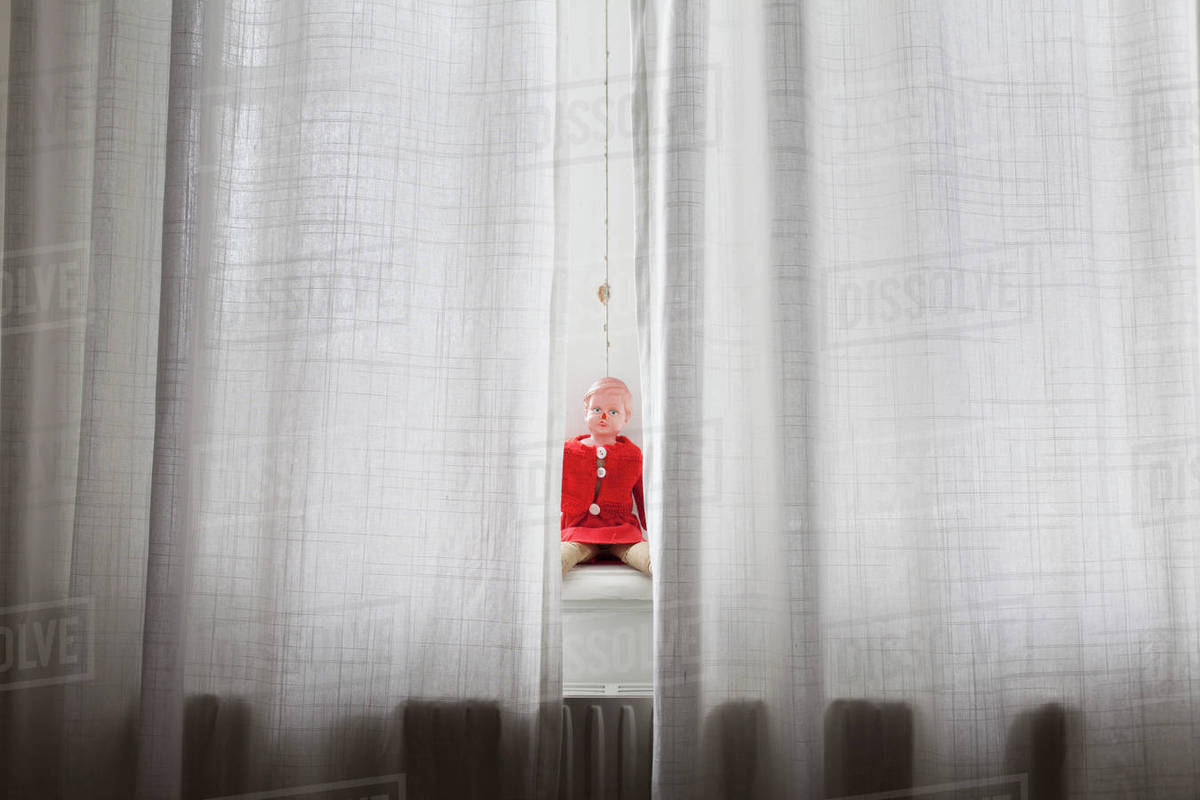 Doll sitting on windowsill behind curtains Royalty-free stock photo