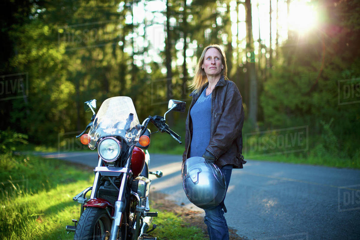 Confident woman standing at motorcycle at roadside in woods Royalty-free stock photo