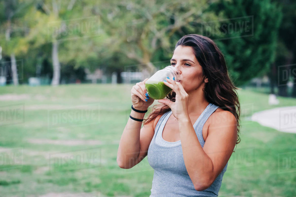 Fit female personal trainer drinking green smoothie in park Royalty-free stock photo