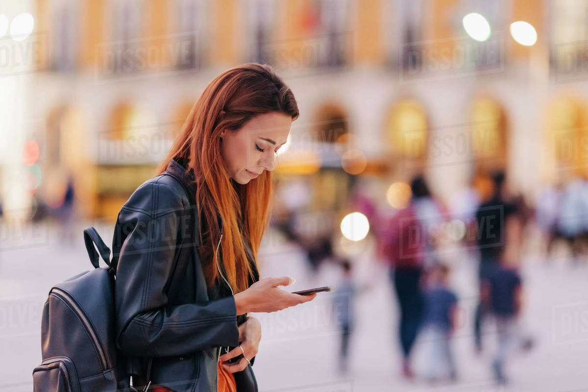 Young woman with backpack using smart phone on urban sidewalk Royalty-free stock photo