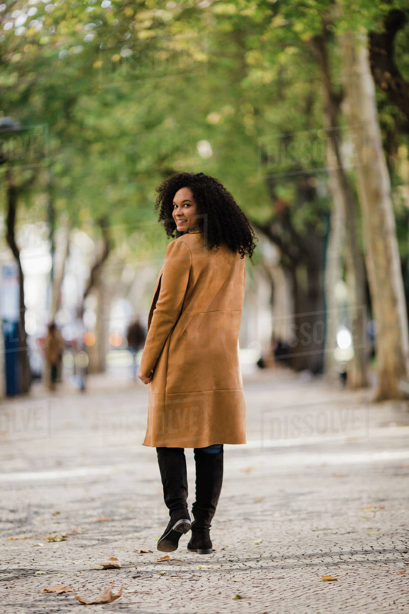 Portrait confident young woman looking over shoulder on treelined sidewalk Royalty-free stock photo