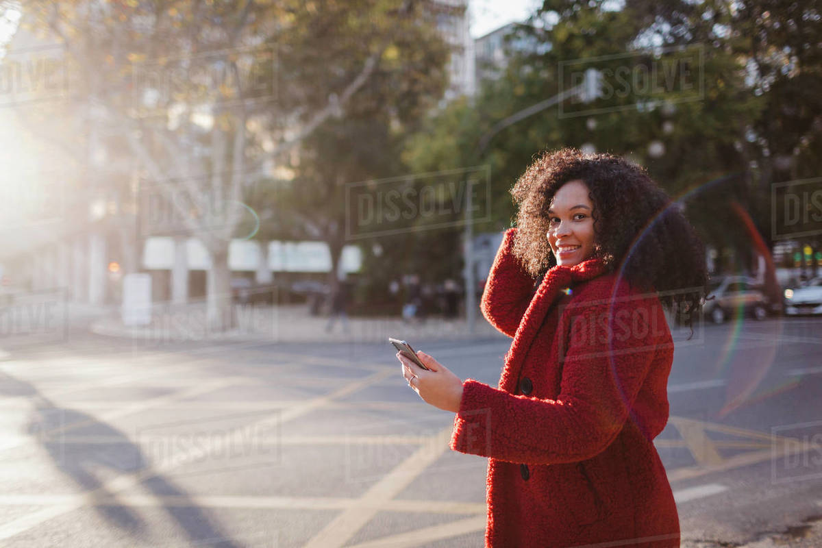 Portrait confident, smiling young woman with smart phone on sunny city street Royalty-free stock photo