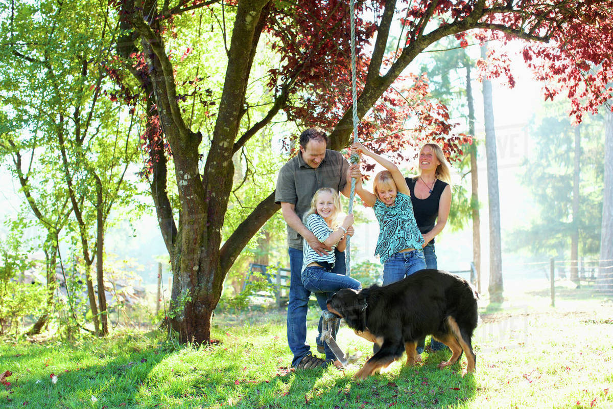 Happy family with dog playing on rope swing in sunny autumn park Royalty-free stock photo